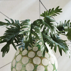 The NAPA HOME AND GARDEN - SPLIT LEAF SELLOUM STEM SMALL offers two green leaves with long stems, serrated edges, and a glossy texture on a white background, tied with a small band, ideal for realistic home decor in curated contemporary settings.