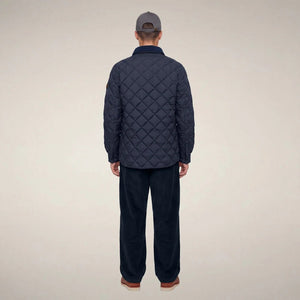 The SAVE THE DUCK - FIRMIN Puffer Jacket in Blue Black by SAVE THE DUCK features a diamond-quilted design, long sleeves, snap button closures, two chest pockets with flaps, and a dark collar, presented against a plain light background.