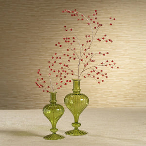 Five green glass vases, including the VENETIAN SPIRAL VASE IN GREEN TURNIP SHAPE by ZODAX and a decorative vase, each with unique shapes and textures, are arranged on a reflective gold tray. Two of the vases are adorned with decorative red berry branches. The softly lit background remains neutral.