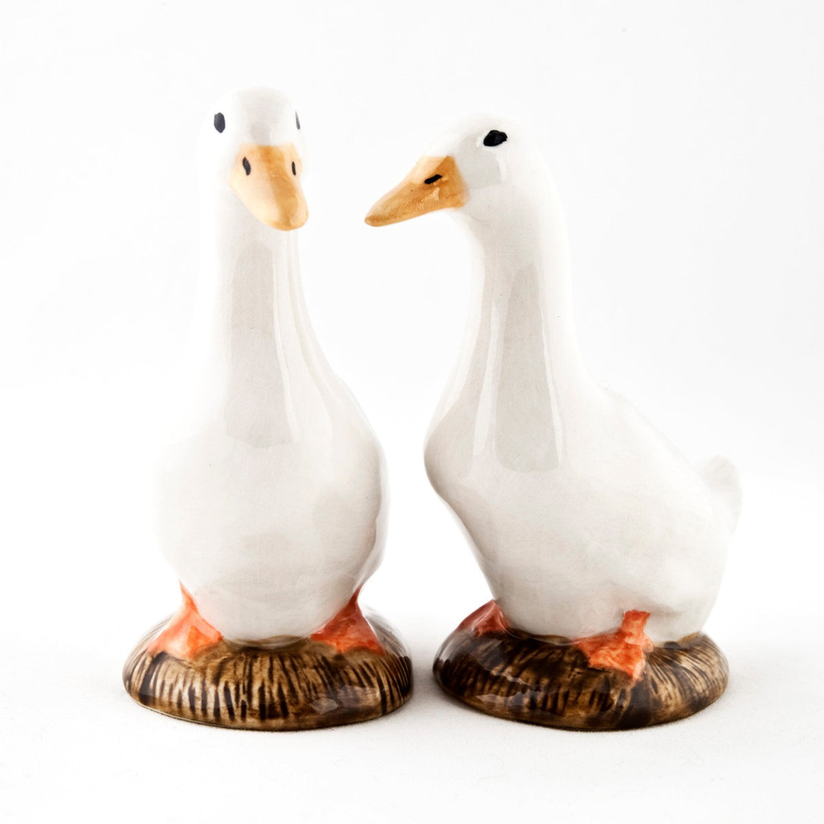 The QUAIL CERAMICS - PEKIN DUCK SALT AND PEPPER SET by QUAIL DESIGNS features two hand-painted stoneware duck figurines with white bodies and orange beaks, standing side by side on brown bases against a plain white background.