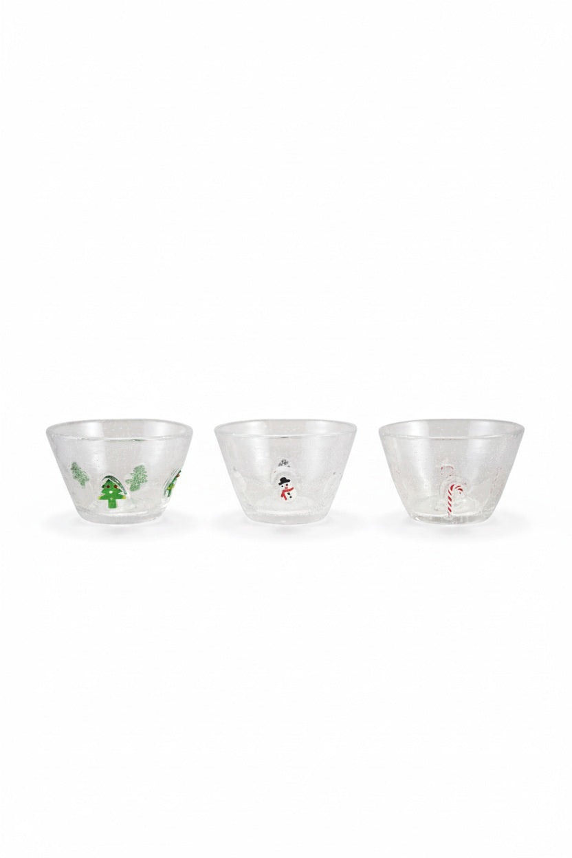 A GLASS BOWL WITH EMBEDDED HOLIDAY ICON filled with granola sits on a wooden table next to a Santa-shaped pitcher and artisan glass tumblers adorned with multicolor icon embellishments.