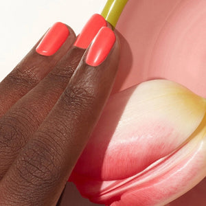 A bottle of MANUCURIST INC’s GREEN™ Nail Polish in the shade “Pulp,” showcasing a vibrant coral hue, with a sleek black cap and a label that reads “green quick dry intense color,” made using bio-sourced ingredients.