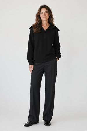 A person seen from behind, wearing a sleek, modern black SAVE THE DUCK - HINATA HALF ZIP TOP with a large collar and dark trousers.