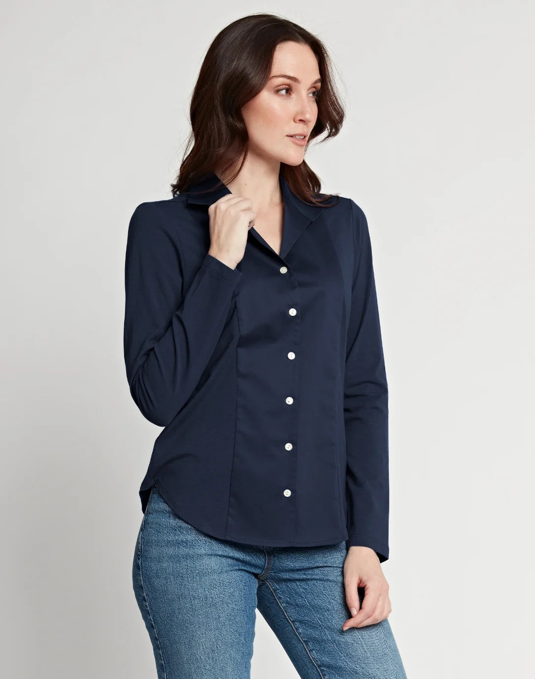 A woman stands against a white wall, wearing the HINSON WU - DONNA Long Sleeve Wing Collar “T” Shirt in navy and black pants. Her hands are relaxed at her sides, and her face is partially out of frame.
