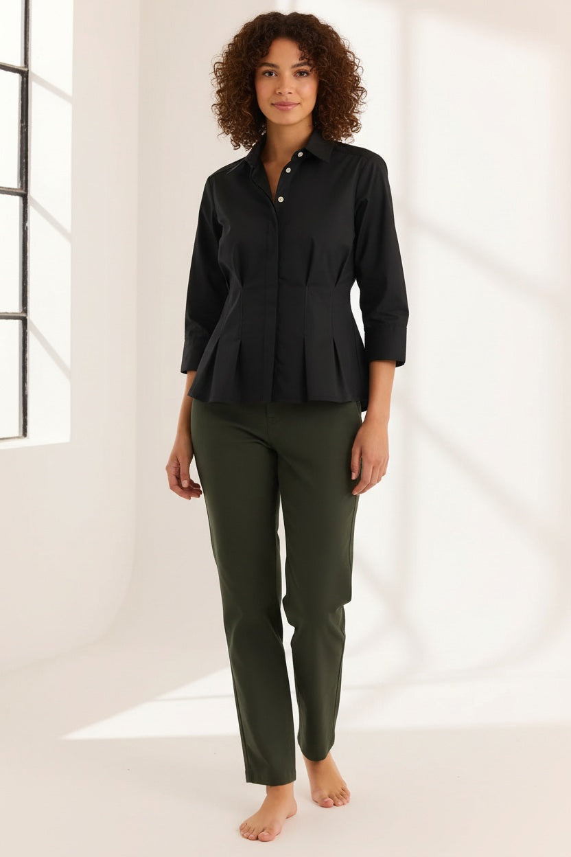 A woman with blonde hair is smiling at the camera while standing against a plain light background, wearing the HINSON WU - MARTINA 3/4 SLEEVE STRETCH POLISHED COTTON SHIRT IN BLACK paired with olive green pants.