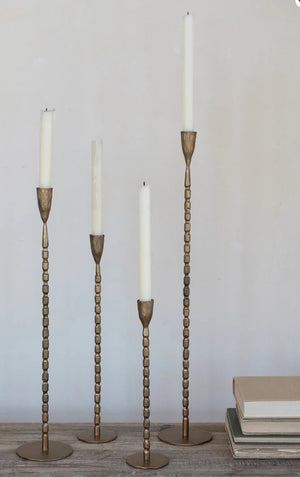 The CREATIVE COOP CAST IRON TAPER HOLDER IN BRASS FINISH, MEDIUM features a sleek, textured stem and round base, bringing elegant style to any setting.