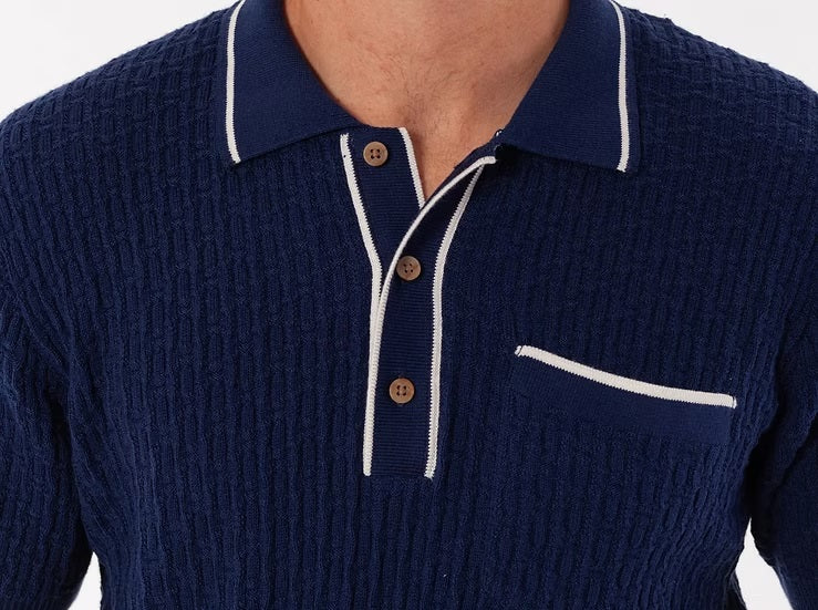 A man models the CRIQUET Bungalow Sweater Polo in navy, featuring white trim on the collar, sleeve cuffs, buttons, and pocket, against a plain white background.