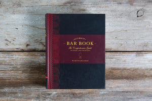 Cover of THE ULTIMATE BAR BOOK: THE COMPREHENSIVE GUIDE TO OVER 1,000 COCKTAILS BY MITTIE HELLMICH from CHRONICLE BOOKS, featuring a brown and olive green design with a wine glass icon—ideal for fans of classic cocktails.