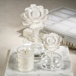 A set of MINI GRANDCASABLANCA PORCELAIN DIFFUSER - 1.7 OZ by ZODAX sit on marble; two display ceramic flower toppers, while others glow softly, filling the air with subtle wild tuberose notes.