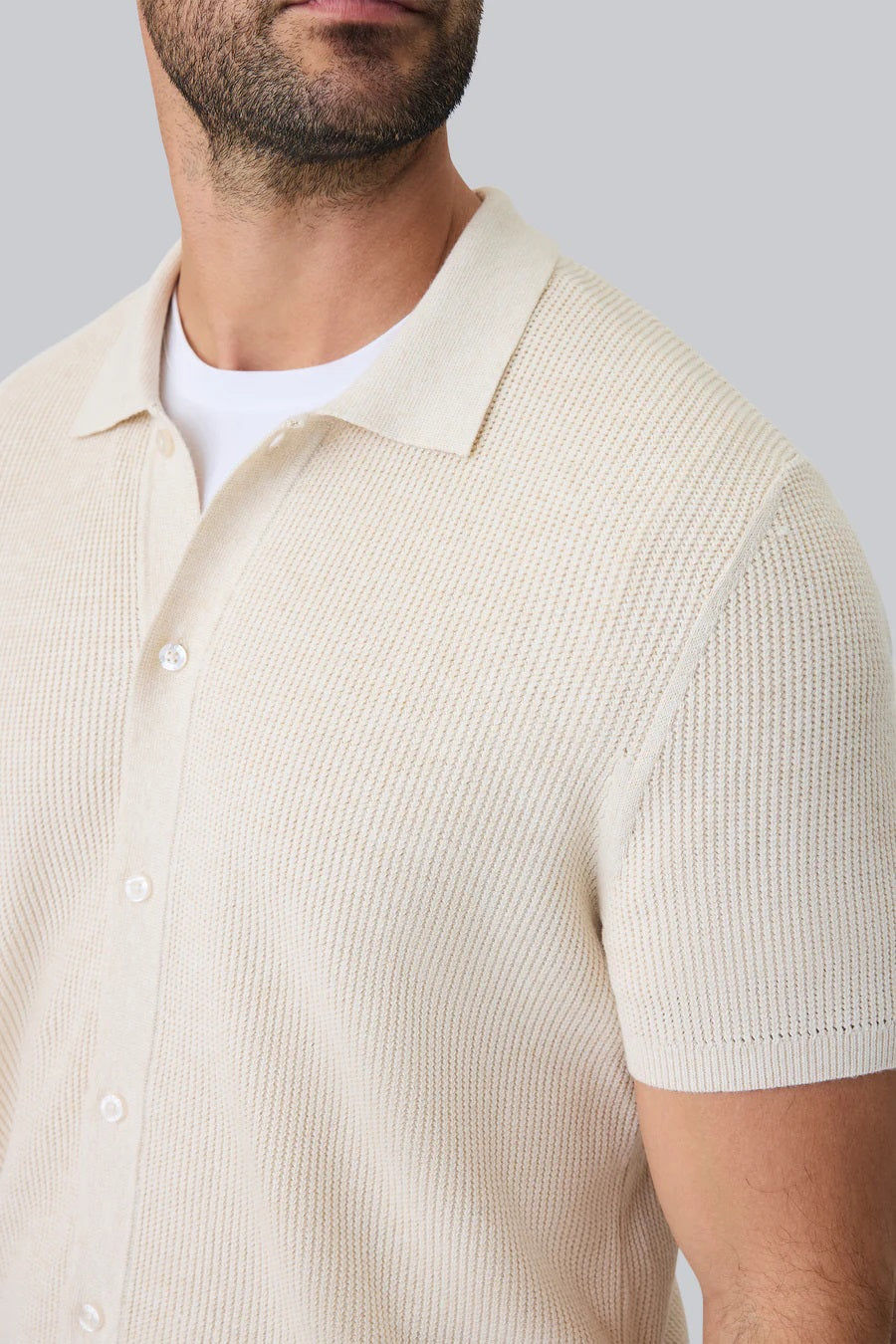 A man with dark hair and a short beard models the MACK WELDON Tech Linen Button Up Sweater Polo in Latte Heather, standing hands-in-pockets against a white background and looking effortlessly stylish and comfortable.
