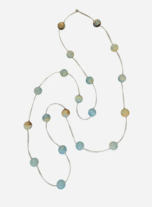 A mannequin in a beige textured sweater showcases the ANN LIGHTFOOT - BLUE CALCITE INTERMITTENT STRAND NECKLACE, a delicate 34" piece with spaced blue and brown beads on a clear strand. The softly blurred background highlights the jewelry.