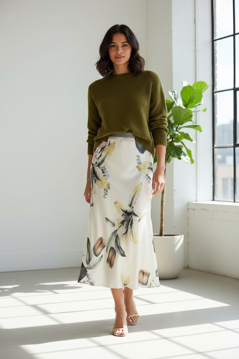 The MIRTO 1956 Botanical Print Midi Skirt features a flowing silhouette, showcasing large, soft-colored flowers and leaves on a light background, complemented by a sleek gray waistband.