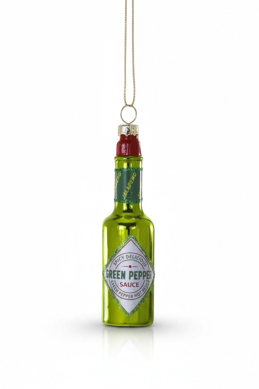 The CODY FOSTER GREEN PEPPER HOT SAUCE ORNAMENT is a shiny green glass decoration shaped like a hot sauce bottle, labeled "Green Pepper Sauce" with a gold hanging loop—ideal for collectors or as a unique gift.