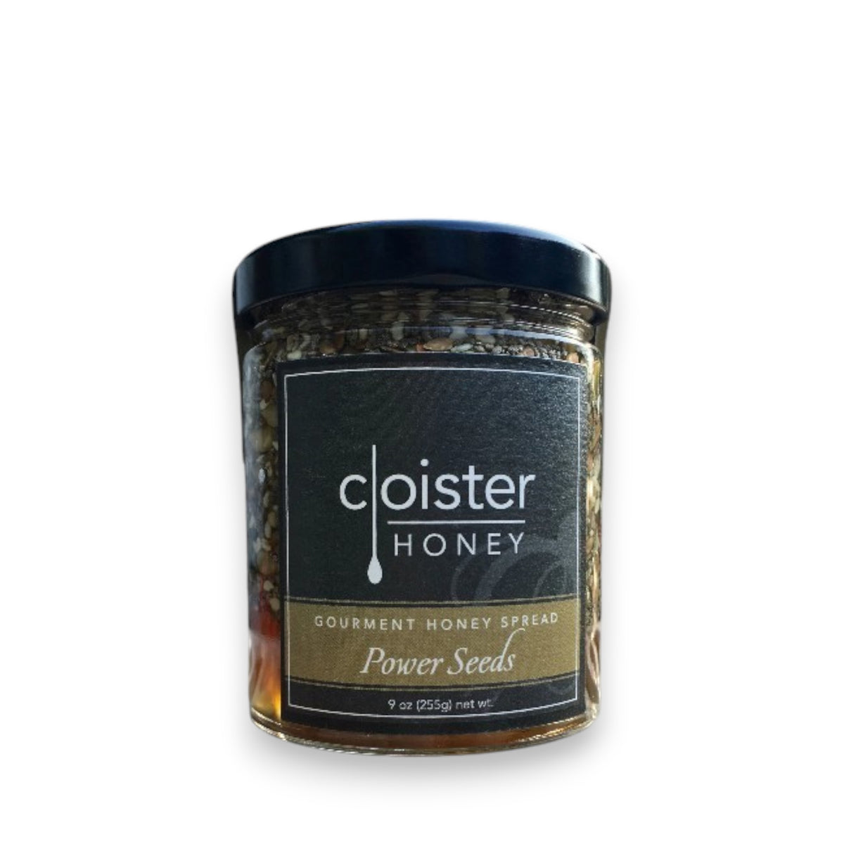 A jar of CLOISTER HONEY - POWER SEED HONEY 9OZ, highlighted for its superfood-enhanced seeds. The transparent jar displays a delectable blend of honey and antioxidant-rich seeds inside. Adorned with a dark label featuring the brand name "CLOISTER HONEY" in white and accented by a gold banner, the jar is capped with an elegant black lid.