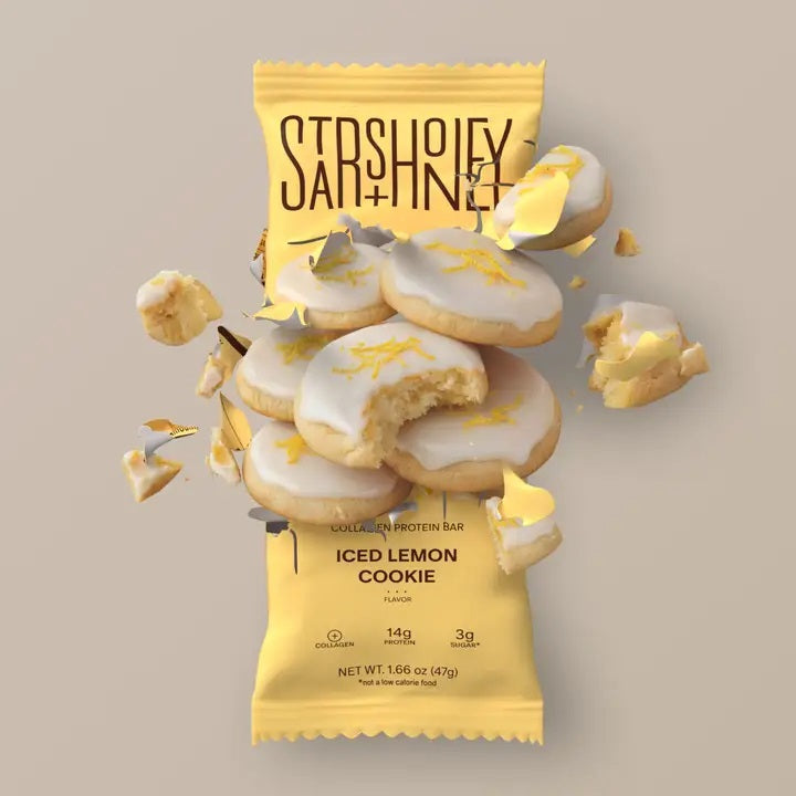 A STARS+HONEY - ICED LEMON COOKIE collagen protein bar in a vibrant yellow wrapper, featuring cookies adorned with white icing and gold sprinkles—some whole, some crumbling—bursting outward against a beige backdrop, capturing a healthy snack from STARS+HONEY packed with delicious flavor.