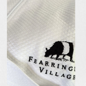 A neatly folded white kimono collar bathrobe adorned with a textured pattern. The bathrobe features an embroidered black bear and the text "Fearrington Village" on the bottom right side. Additionally, it boasts adjustable belt loops for a perfect fit. The label inside the collar reads "F".