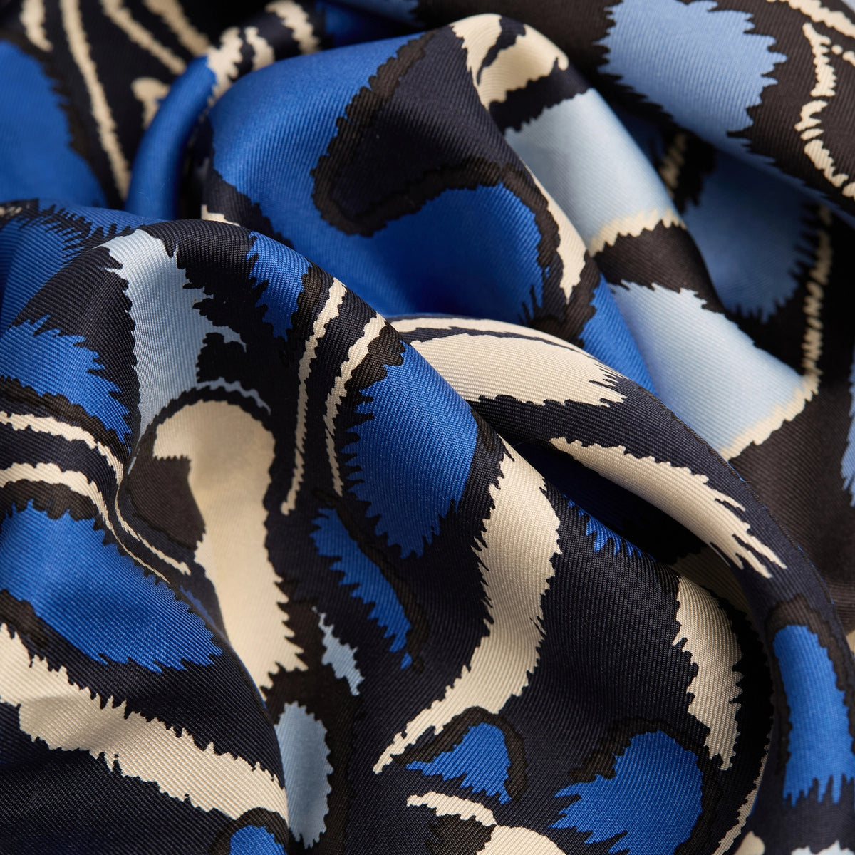 A close-up of the INOUI EDITIONS PAPILLON silk scarf in blue, featuring a smooth, shiny texture and abstract butterfly-inspired pattern in blue, black, and cream—a versatile accessory crafted in India by INOUI.