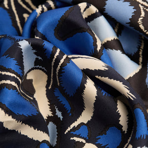 A close-up of the INOUI EDITIONS PAPILLON silk scarf in blue, featuring a smooth, shiny texture and abstract butterfly-inspired pattern in blue, black, and cream—a versatile accessory crafted in India by INOUI.
