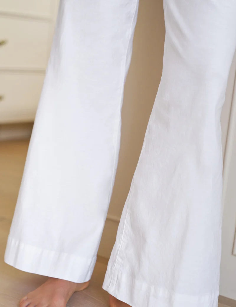 A person in FRANK & EILEEN’s WEST VILLAGE WIDE LEG LINEN TROUSER IN WHITE stands barefoot on a light floor by pale furniture, capturing effortless NYC style.