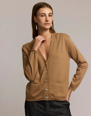 A woman with straight brown hair wears the HINSON WU CASSIE Long Sleeve Cotton Silk Cardigan in camel, styled with black pants. She poses confidently, one hand to her chin, against a neutral backdrop.