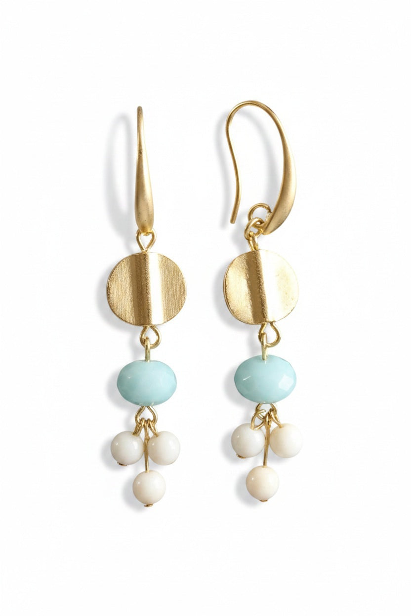 The DAVID AUBREY - AMAZONITE AND GLASS EARRINGS by DAVID AUBREY feature a round gold disk, a light blue amazonite bead, and three small white glass beads hanging from each earring, creating an elegant blend of classic style and contemporary charm against a striking black background.