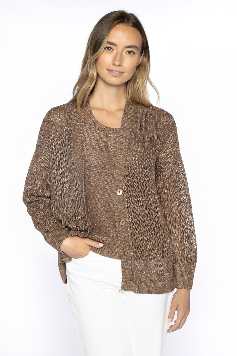 A woman with long, light brown hair wears the KINROSS CASHMERE Open Texture Lurex Linen Cardigan over a matching top and white pants. She stands against a white background, one hand in her pocket, smiling softly.
