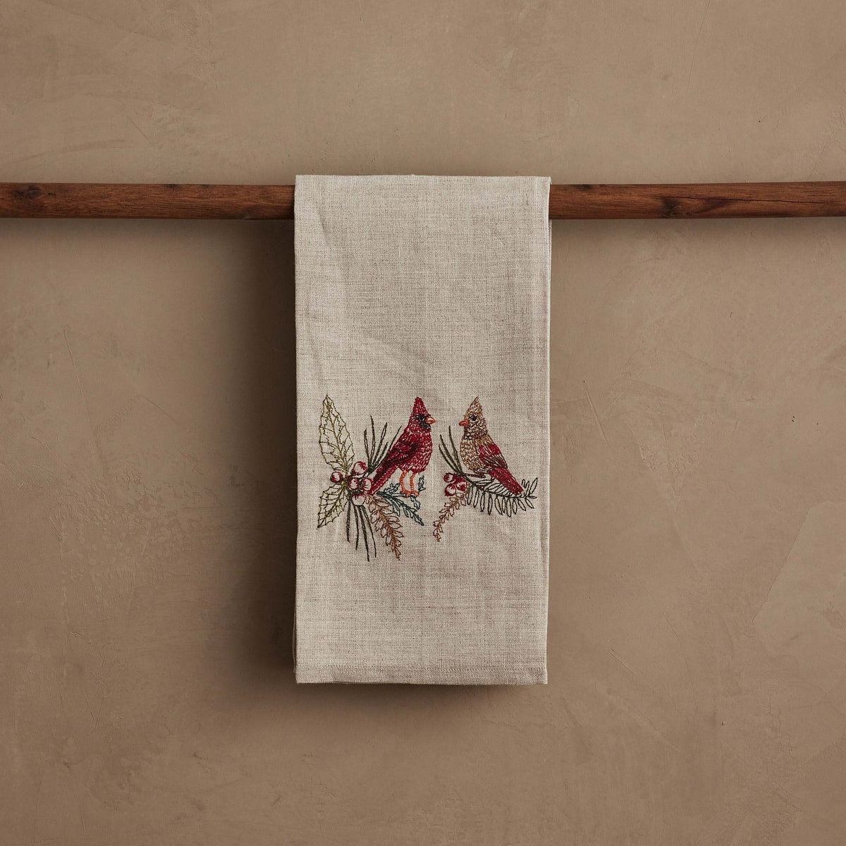 A CORAL & TUSK CHRISTMAS CARDINALS LINEN TEA TOWEL made of embroidered natural flax fiber featuring two cardinals perched on pine branches with berries.