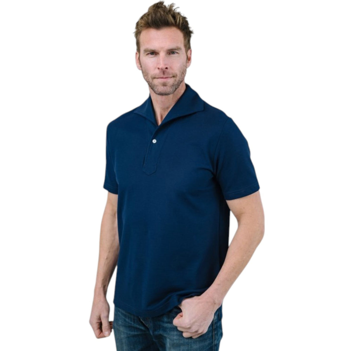 A man with light brown hair and a short beard wears the EDWARD ARMAH Pima Cotton Tailored Polo Shirt in dark blue and jeans, standing against a plain light background with a relaxed expression and one hand in his pocket.
