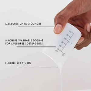 The LAUNDRESS - MEASURING CUP by THE LAUNDRESS is a white plastic measuring cup featuring ounce and milliliter markings on the side, making it ideal for accurately measuring THE LAUNDRESS detergents and other fabric care products.