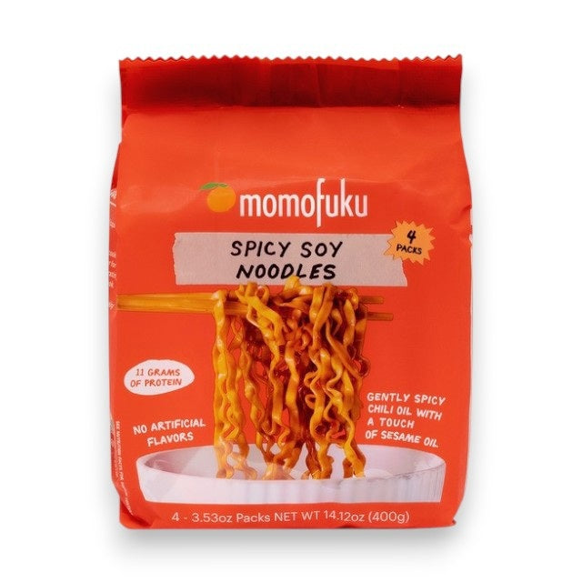A bright orange bag of MOMOFUKU - SPICY SOY NOODLES shows a bowl of air-dried noodles, notes five packs inside, no artificial ingredients, and a net weight of 16.75 oz (1.05 lb).