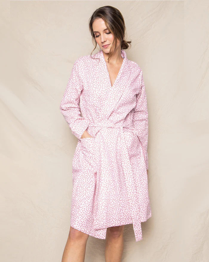 The PETITE PLUME - SWEETHEARTS ROBE by PETITE PLUME is a luxurious bathrobe that showcases a delightful small floral print pattern in pink and white. Crafted from the finest quality cotton, this elegant robe features long sleeves, a shawl collar, and a matching belt tied at the waist. The soft and comfortable fabric makes it perfect for lounging in style.