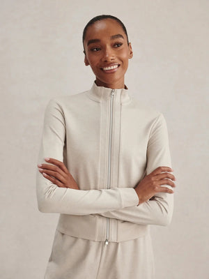 A person wears a light beige Varley Rufus Cropped Zip Through Sweat in Pebble Marl with a high collar and matching pants.