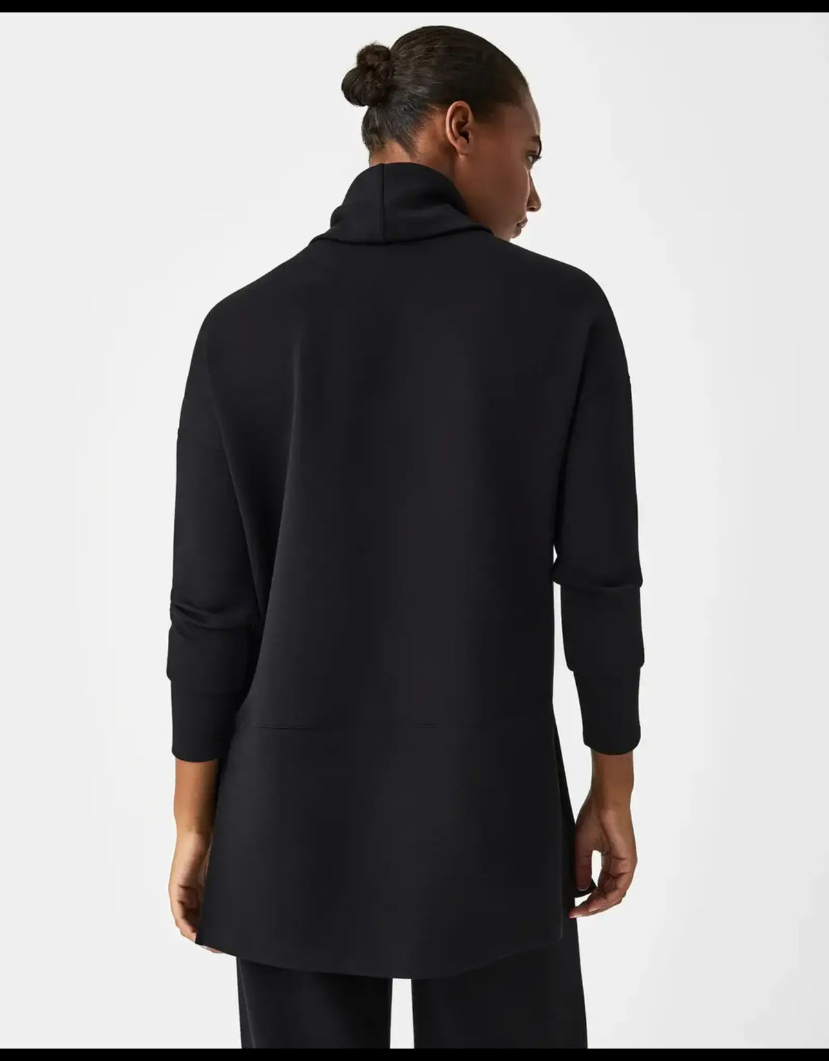 A person pulls up the collar of the SPANX - AIRESSENTIALS TURTLENECK TUNIC IN BLACK, smiling with closed eyes against a plain light background—perfectly showcasing the brand&#39;s light-as-air fabric and playful style.