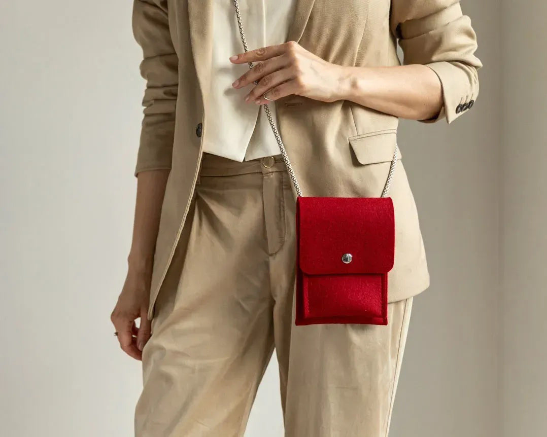 A person in a loose gray shirt and taupe pants carries the WOOLBERRY WOOL FELT PHONE BAG—a pink crossbody with a flap and silver chain—over their shoulder, showing only their torso and part of their arms.