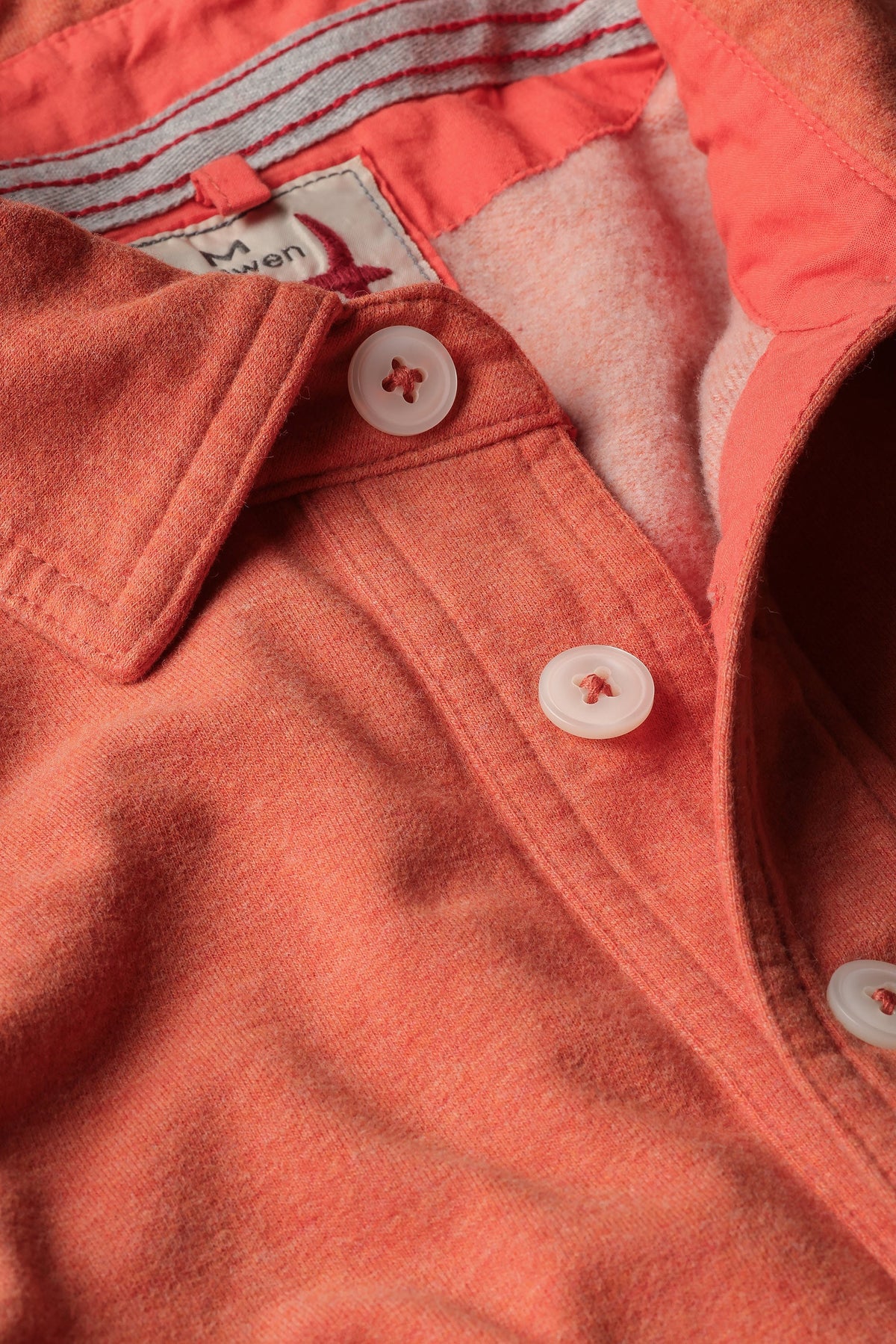 Close-up of the RELWEN Mariner Polo in Orange Fade, crafted from soft French terry, featuring white buttons, a collar, and a glimpse of the inner tag with striped fabric detail.
