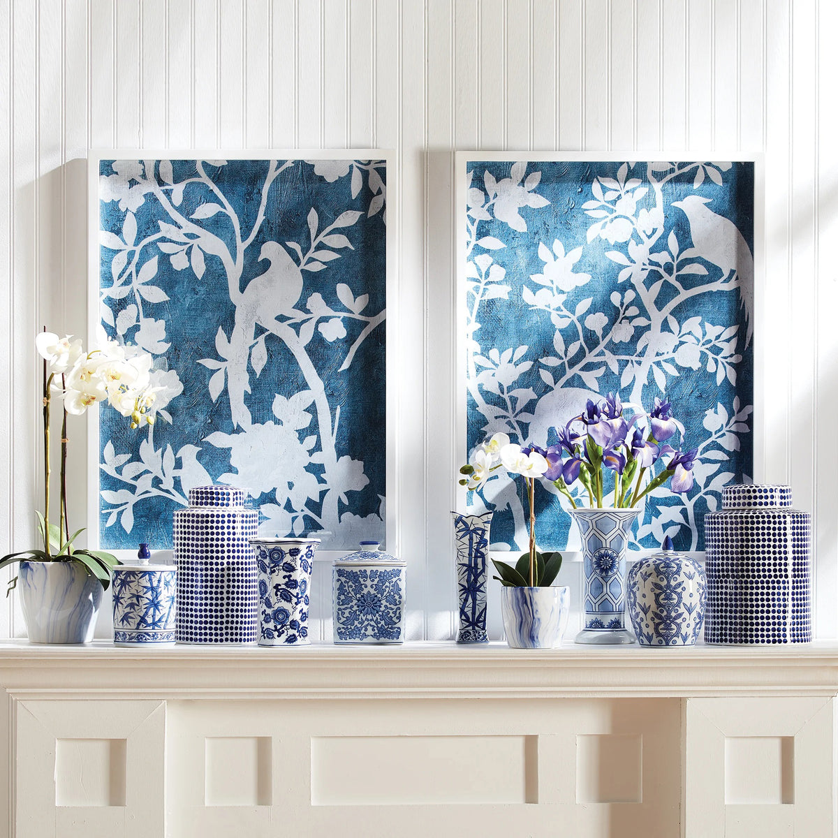 NAPA HOME AND GARDEN&#39;s &quot;Aviary Cyano&quot; prints showcase silhouettes of birds on tree branches in a textured blue backdrop, with intricately detailed white leaves and blossoms, offering a serene, nature-inspired aesthetic.