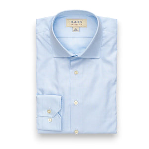 The HAGEN - COTTON DRESS SHIRT IN SKY MINI HOUNDSTOOTH features a modern spread collar, white buttons, and premium cotton fabric. The neatly folded shirt displays the Hagen label and comes in a light blue mini houndstooth pattern.