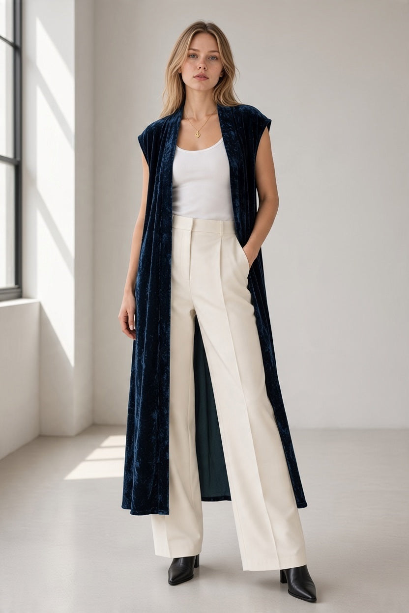 A person wears a GAYNOR BONGARD - POETA VELVET GILET IN MIDNIGHT over a white tank top and cream-colored wide-leg trousers for a look of dramatic elegance.