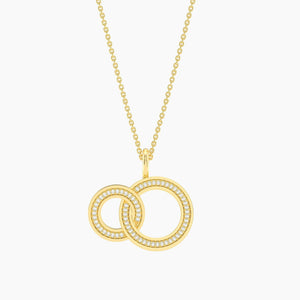 The ELLA STEIN - FOREVER LINKED PENDANT NECKLACE by ELLA STEIN features two interlocking circle pendants, each adorned with sparkling gemstones, suspended from a delicate gold-plated stainless steel chain and displayed against a white background.