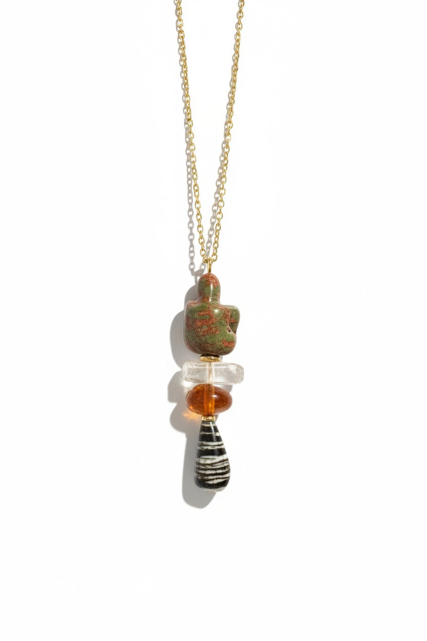 Introducing the SANDRINE FRANCE - COMPANION BLAKE NECKLACE by SANDRINE FRANCE STUDIO—a stunning 22-inch gold chain charm necklace, featuring a pendant with four distinct, stacked beads: a green irregular stone, a clear crystal, an amber disc, and a black-and-white striped teardrop bead. This standout piece of jewelry adds an elegant and unique touch to any outfit.