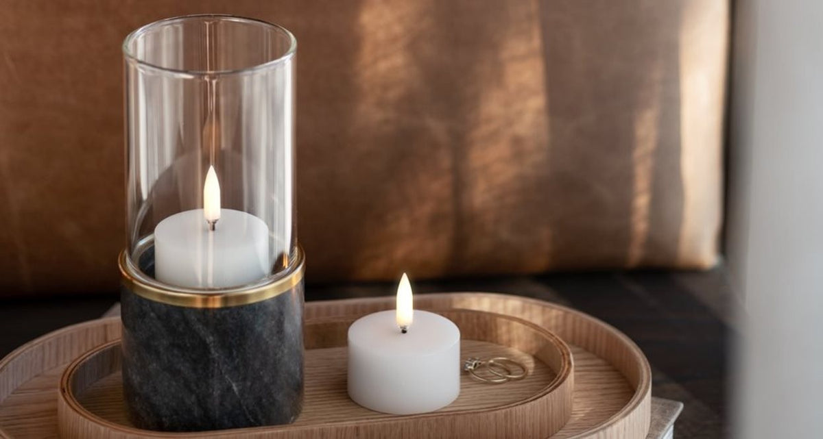 A compact, ivory UYUNI pillar candle (2x1.1) by PIFFANY with a glowing central flame, displayed against a simple white background.