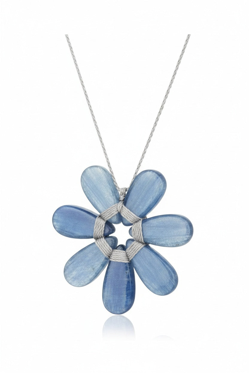 The ANN LIGHTFOOT Seven Petal Kyanite Flower Necklace features a pendant shaped like a flower with seven glossy blue kyanite petals, intricately wrapped together with light-colored cord and suspended from a delicate silver chain.