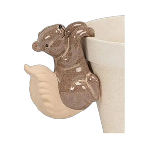 A brown ceramic CLIMBING SQUIRREL POT HANGER by ABBOTT perched on the rim of a planter.