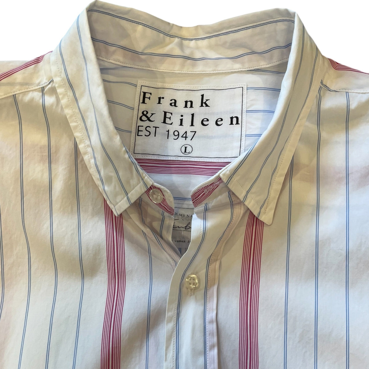 A man in a FRANK &amp; EILEEN Finbar Men's Button Up Shirt in hot pink and blue stripe, blue jeans, and white sneakers walks confidently down a cobblestone street lined with stone buildings and potted plants on a sunny day.