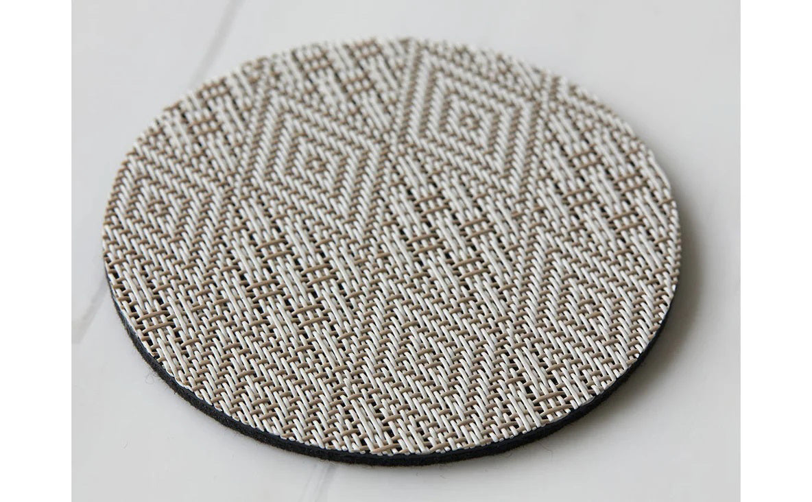 The CHILEWICH Boxwood Round Coasters Set of 4 features woven beige and white coasters with a subtle geometric pattern, combining style and function to protect your table. One holds a clear glass tumbler, all arranged on a white surface.