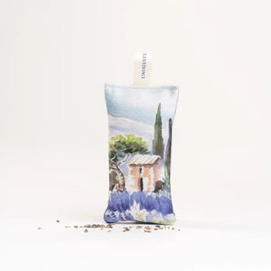 The L'AUGUSTE PROVENCE - FRENCH LAVENDER SACHET FROM PROVENCE is a small handcrafted pouch with a countryside watercolor design, upright shape, "L'AUGUSTE PROVENCE" tag, and dried lavender pieces at its base.