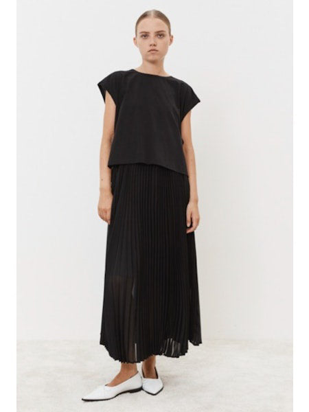 Against a plain white backdrop, a person models the MEIMEIJ Navy Plisse Dress. Paired with white pointed shoes, this minimalistic ensemble epitomizes versatile style. Their expression is neutral, enhancing the understated elegance of the look.