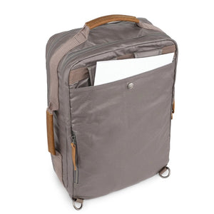 A close-up of the TSD BRAND - MADRONE Coated Canvas Backpack in Grey shows its brown leather accents and an unzipped front pocket with a black wallet partially visible inside.