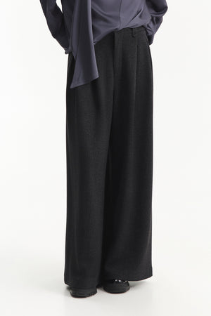 A person is shown from the shoulders down against a plain white background, wearing ELEH - BLACK PALAZZO TROUSERS by ELEH styled with black shoes and a loose-fitting, long-sleeve top.