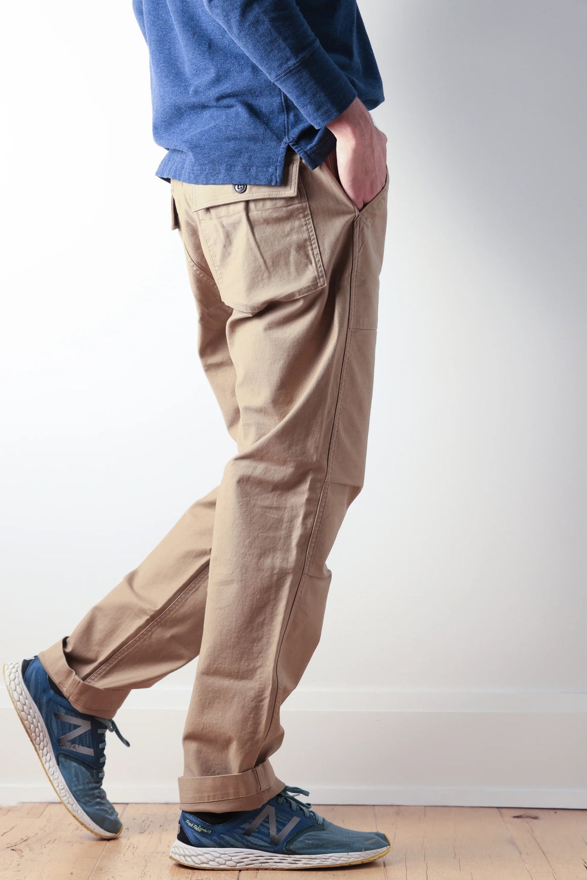 The RELWEN Supply Pant in Worker Khaki is a pair of light brown chinos inspired by classic military utility pant design, featuring side adjuster tabs, a button fly, broken twill fabric, and cuffs at the ankles with a subtly tapered leg silhouette—laid flat on a white background.